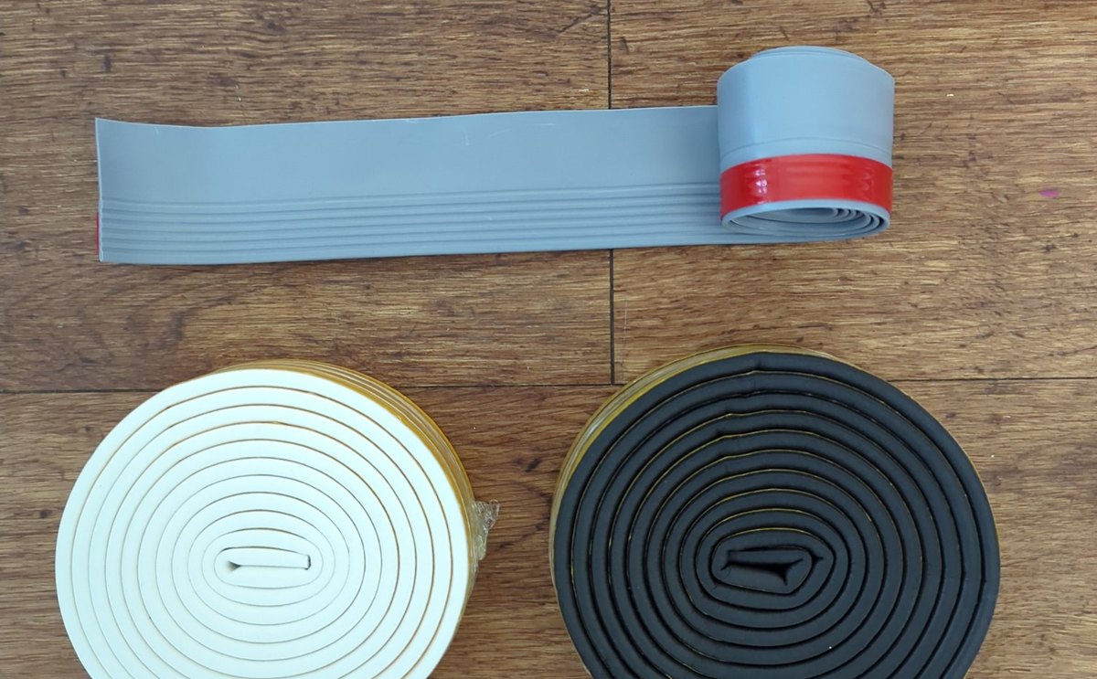 The Hallhush Room Kit laid out on a wood floor: a grey door-bottom strip and two rolls of seal.